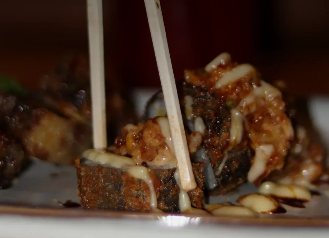 Hashi pegando um pedaço de um roll de sushi crocante, com molho