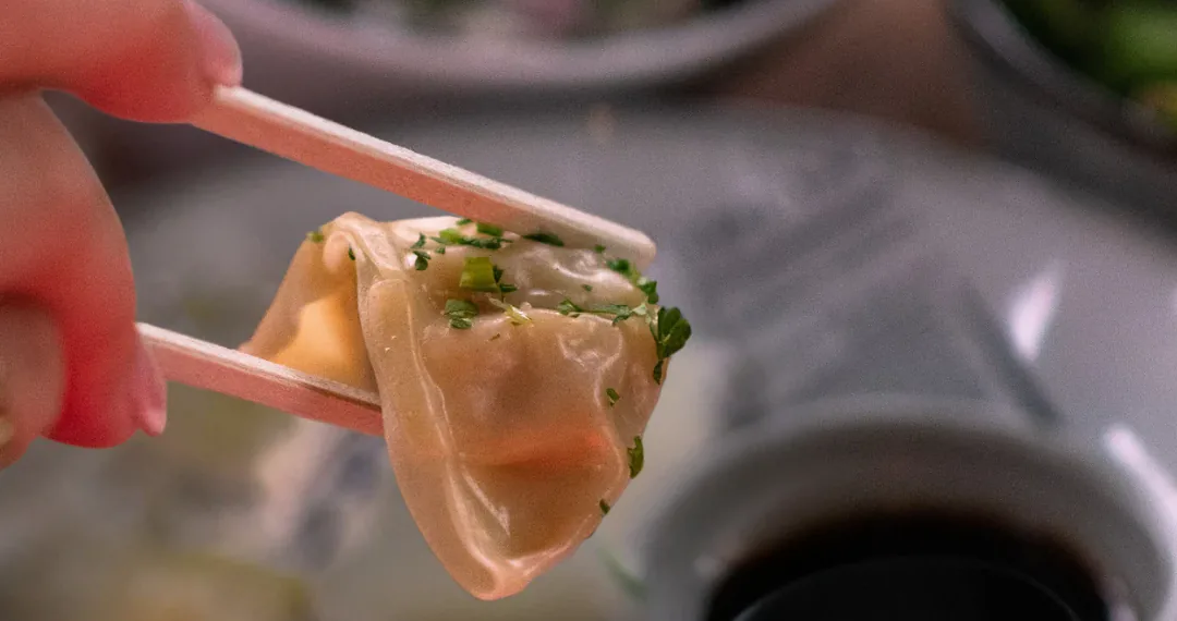 Um gyoza dourado na frigideira, segurado com hashi sobre um pratinho de shoyu