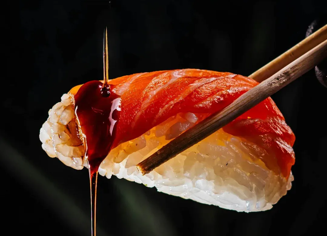 Nigiri de salmão erguido com hashi sobre um fundo escuro