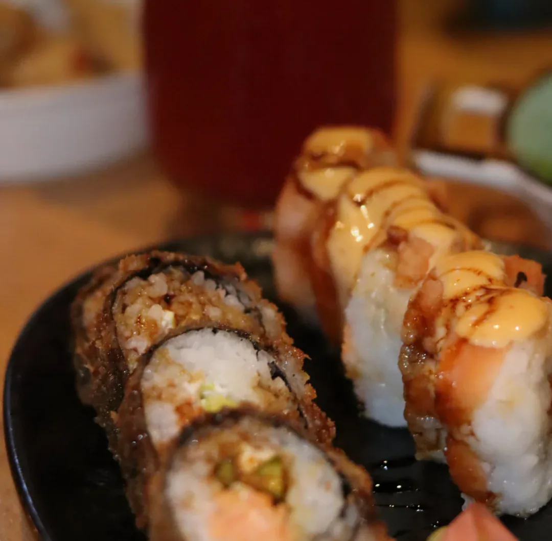 Dois rolls especiais em um prato escuro: um roll crocante de tempurá e um roll de salmão maçaricado com calda